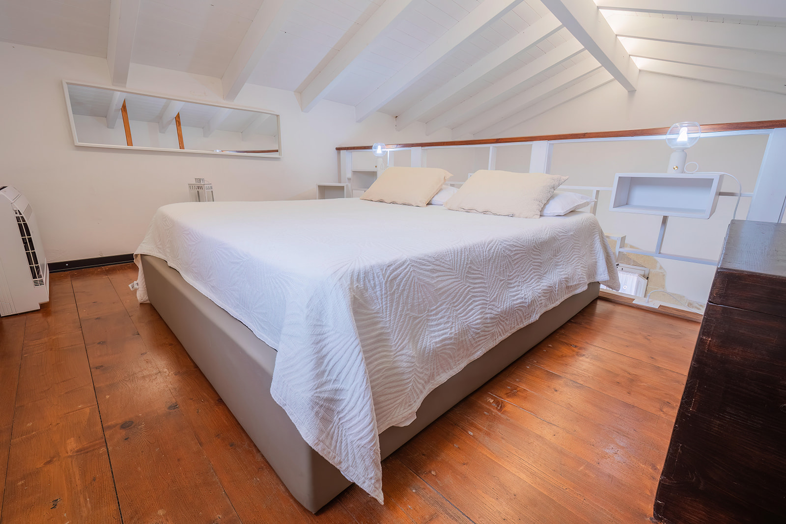 Camera matrimoniale sul soppalco con tetto a falde e travi bianche