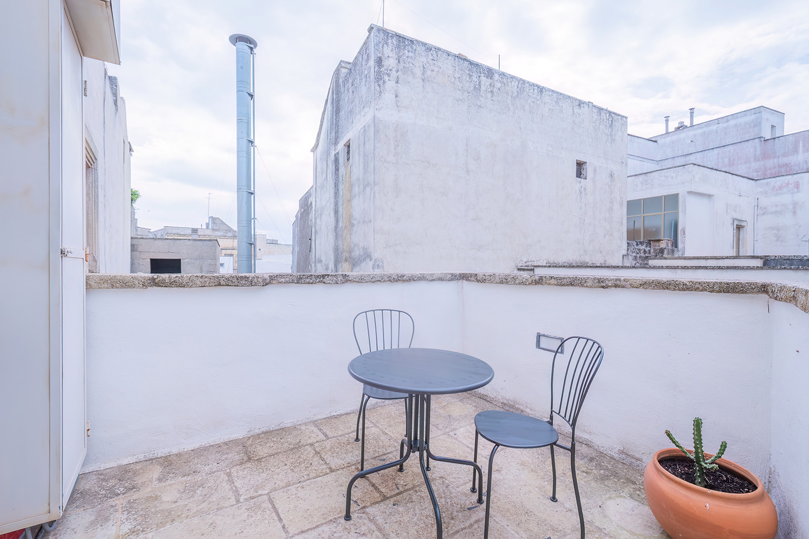 Terrazzino bianco con tavolino in ferro e vista sui tetti del centro storico di Corigliano d'Otranto
