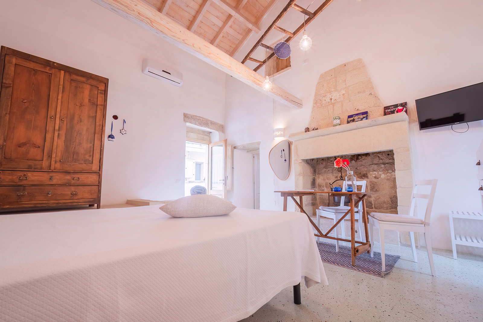 Soggiorno-camera della Dimora 3 con camino in pietra, soffitto a falda con travi e scaletta decorativa appesa