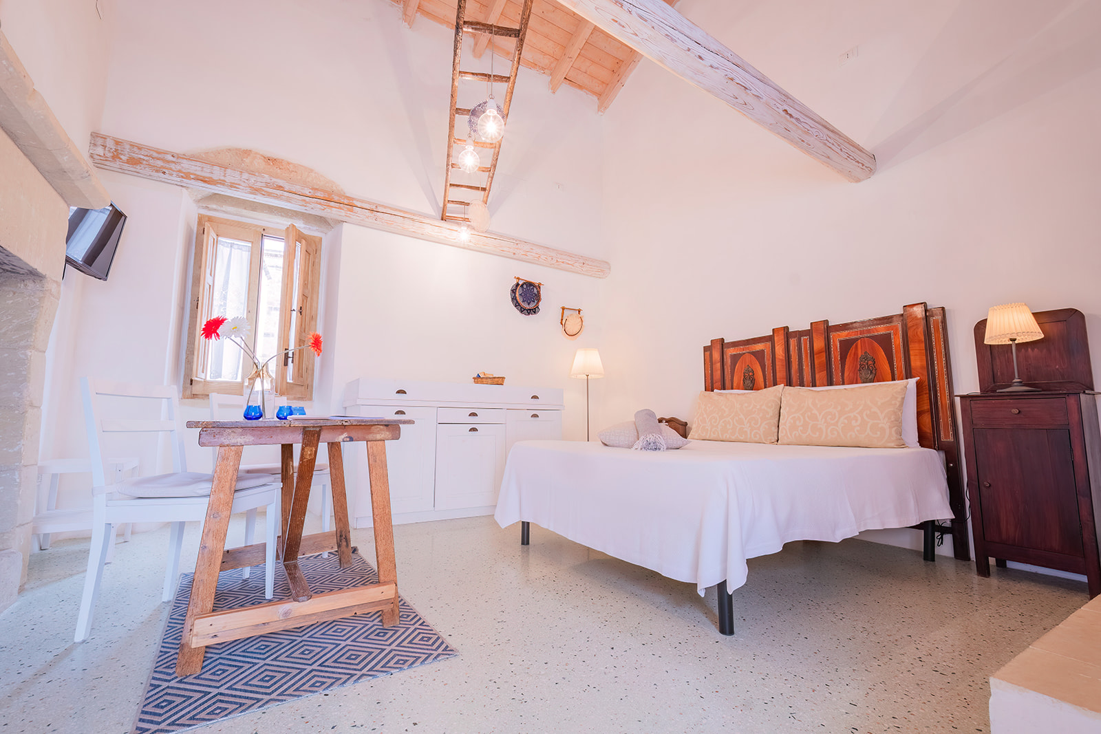 Letto matrimoniale della Dimora 3 con testata antica intarsiata e tavolino in legno grezzo